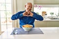 Senior man with grey hair eating pasta spaghetti at home smiling in love doing heart symbol shape with hands Royalty Free Stock Photo