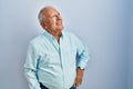 Senior man with grey hair standing over blue background looking away to side with smile on face, natural expression Royalty Free Stock Photo