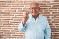 Senior man with grey hair standing over bricks wall showing and pointing up with fingers number two while smiling confident and Royalty Free Stock Photo
