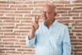 Senior man with grey hair standing over bricks wall smiling looking to the camera showing fingers doing victory sign Royalty Free Stock Photo