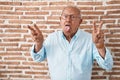 Senior man with grey hair standing over bricks wall smiling with tongue out showing fingers of both hands doing victory sign Royalty Free Stock Photo