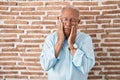 Senior man with grey hair standing over bricks wall tired hands covering face, depression and sadness, upset and irritated for