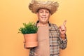 Senior man with grey hair wearing gardener hat holding plant pot smiling happy pointing with hand and finger to the side Royalty Free Stock Photo