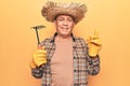 Senior man with grey hair wearing gardener hat holding rake smiling happy pointing with hand and finger to the side Royalty Free Stock Photo