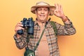 Senior man with grey hair wearing hiker bakcpack holding binoculars doing ok sign with fingers, smiling friendly gesturing Royalty Free Stock Photo