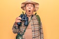 Senior man with grey hair wearing hiker bakcpack holding binoculars scared and amazed with open mouth for surprise, disbelief face Royalty Free Stock Photo