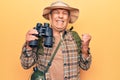 Senior man with grey hair wearing hiker bakcpack holding binoculars screaming proud, celebrating victory and success very excited