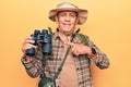 Senior man with grey hair wearing hiker bakcpack holding binoculars smiling happy pointing with hand and finger Royalty Free Stock Photo