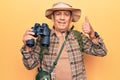 Senior man with grey hair wearing hiker bakcpack holding binoculars smiling happy and positive, thumb up doing excellent and Royalty Free Stock Photo