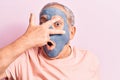 Senior man with grey hair wearing mud mask peeking in shock covering face and eyes with hand, looking through fingers afraid Royalty Free Stock Photo