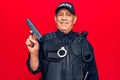 Senior man with grey hair wearing police uniform holding gun looking positive and happy standing and smiling with a confident