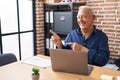 Senior man with grey hair working using computer laptop at the office smiling and looking at the camera pointing with two hands Royalty Free Stock Photo