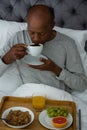 Senior man having breakfast while sitting on bed Royalty Free Stock Photo