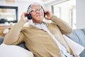 Senior man, headphones and listening to music in home, living room and relax on lounge sofa with podcast, radio or sound Royalty Free Stock Photo