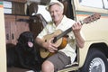 Senior Man With His Dog Playing Guitar In Campervan