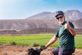 Senior man on his electro bike in outdoor excursion gesturing positive sign with tumb up. Sporty helmet and sunglasses. Green Royalty Free Stock Photo