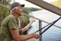 Senior man with his grandson sitting on wooden pontoon with fishing rods in hands, enjoying beautiful nature, little boy pointing Royalty Free Stock Photo