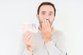 Senior man holding fifty pounds bank note over isolated background cover mouth with hand shocked with shame for mistake,