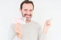 Senior man holding fifty pounds bank note over isolated background very happy pointing with hand and finger to the side