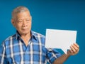 Senior man holding and looking at a blank paper speech bubble while standing on a blue background Royalty Free Stock Photo