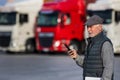 Senior man logistician with phone standing in front of trucks