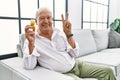 Senior man holding pills smiling looking to the camera showing fingers doing victory sign Royalty Free Stock Photo