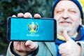 Senior Man is holding a smartphone with logo of UEFA Euro 2020 on screen