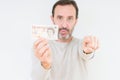Senior man holding ten pounds bank note over isolated background pointing with finger to the camera and to you, hand sign,