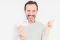 Senior man holding ten pounds bank note over isolated background very happy pointing with hand and finger to the side