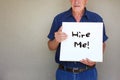 Senior man holding white canvas board in front of his face with the phrase hire me! Royalty Free Stock Photo