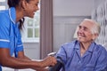 Senior Man At Home In Bed Having Blood Pressure Taken By Female Care Worker In Uniform