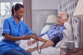 Senior Man At Home In Bed Having Blood Pressure Taken By Female Care Worker In Uniform