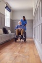 Senior Man At Home Being Pushed In Wheelchair By Female Care Worker In Uniform