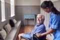 Senior Man At Home Being Pushed In Wheelchair By Female Care Worker In Uniform