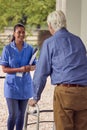 Senior Man At Home Using Walking Frame Greeting Female Nurse Or Care Worker In Uniform At Door Royalty Free Stock Photo