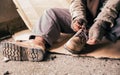 Senior man homeless wearing sweater and cloth gloves with sitting on cardboard and tying laces on shoes