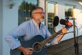 Senior man imposing musician plays the guitar and sings into microphone. Elegant elderly male 60 bearded performs outdoors in