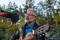 Senior man imposing musician plays the guitar and sings into microphone. Elegant middle aged male bearded performs outdoors on