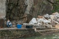 Senior man with large white beard sitting at bottom of rock face looking up from reading newspaper