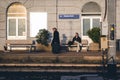 Senior man is leaving train station while young man is sitting on a bench near station platform.