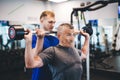 Senior man lifting weights with help of gym assistant.