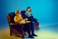 Senior man and little girl, grandfather watching TV with his granddaughter over blue background in neon light Royalty Free Stock Photo