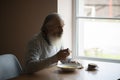 Old sad man with a long gray beard sitting by the table and eating soup and bread Royalty Free Stock Photo