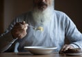 Old sad man with a long gray beard sitting by the table and eating soup and bread Royalty Free Stock Photo