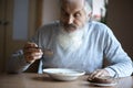 Old sad man with a long gray beard sitting by the table and eating soup and bread Royalty Free Stock Photo