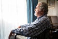 Senior man looking through window while sitting on wheelchair in retirement home Royalty Free Stock Photo
