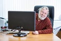 Senior man looks out from behind the monitor, sitting at the office desk, glasses on his forehead Royalty Free Stock Photo