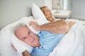 Senior man lying on bed and covering his ears with pillow Royalty Free Stock Photo