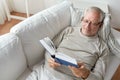 Senior man lying on sofa and reading book at home Royalty Free Stock Photo