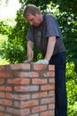 Senior man is making a chimney of red bricks, working with a trowel and making masonry works, vertical Royalty Free Stock Photo